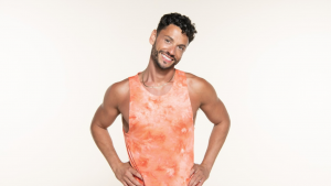 Leroy is wearing an orange tie-dyed vest and smiling into the camera with both hands on his hips. 