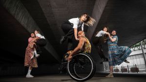 Six dancers from Stopgap’s outdoor show Frock, in three pairs, they are caught mid-air in a moment where three are lifted up by their partner, they dance outside under an urban underpass.